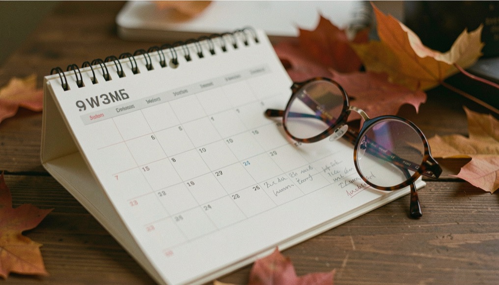Paper calendar turned toward autumn weeks with penciled marks beside resting round spectacles